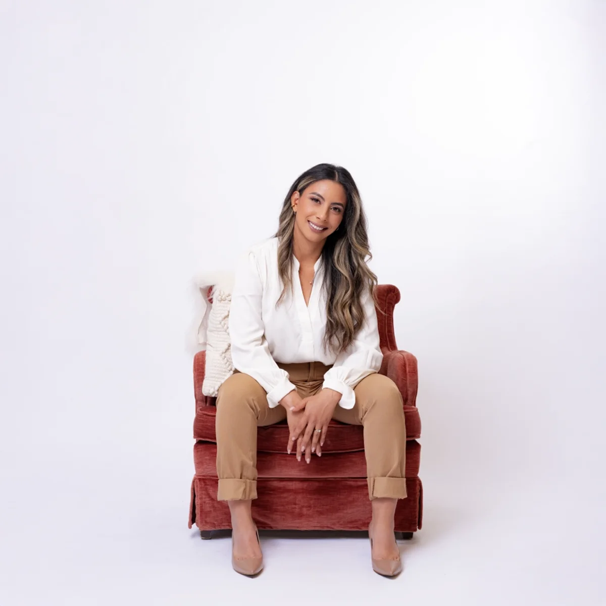 Brunette woman in a white shirt sitting in a red chair.