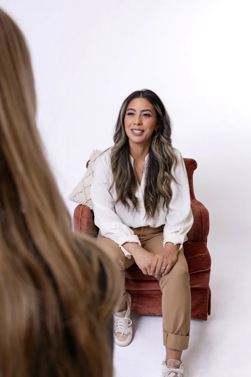 Woman in a white shirt sitting in a red chair to another person.